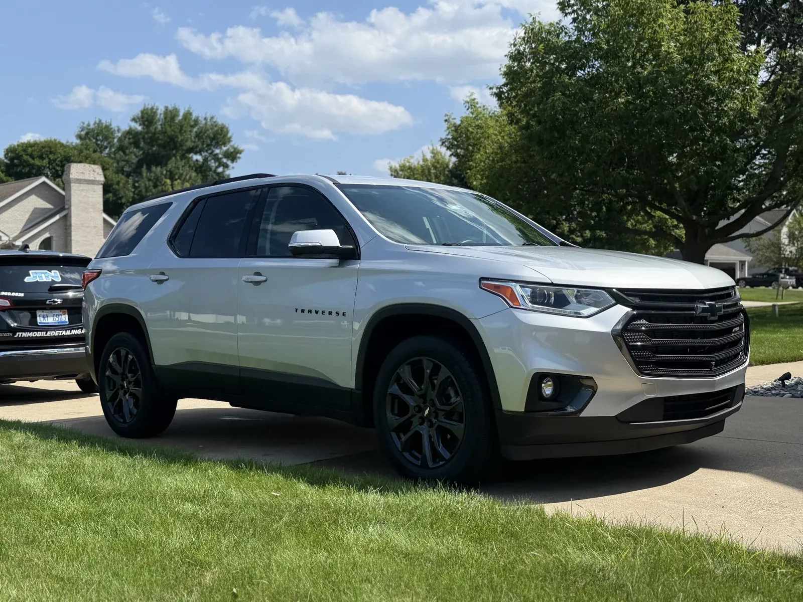 Silver Chevy Traverse after a driveway mobile detail, with a JTN Mobile Detailing unit parked behind
